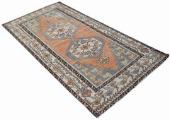 A vintage handwoven Persian rug featuring geometric medallions in blue and orange on a cream field.