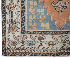 A vintage handwoven Persian rug featuring a geometric floral pattern in blue, orange, and cream.