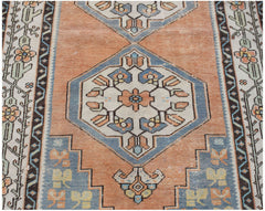 A vintage handwoven Persian rug featuring a geometric floral pattern in orange, blue, and cream.