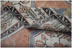 A folded vintage Persian rug featuring a floral pattern in orange, blue, and cream tones.