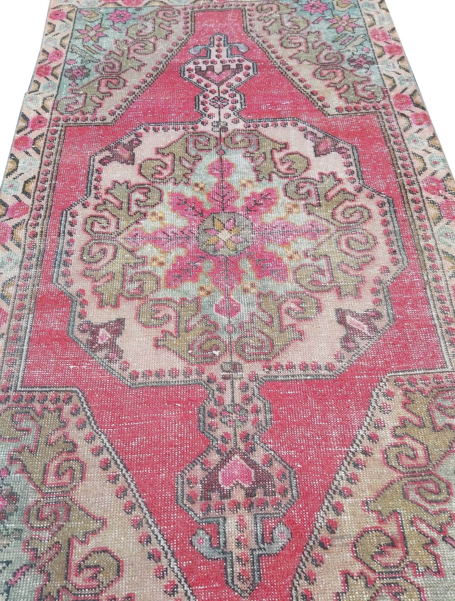 A vintage handmade Turkish wool rug featuring a central medallion in shades of pink, green, and tan.