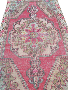 A vintage handmade Turkish wool rug featuring a central medallion in shades of pink, green, and tan.