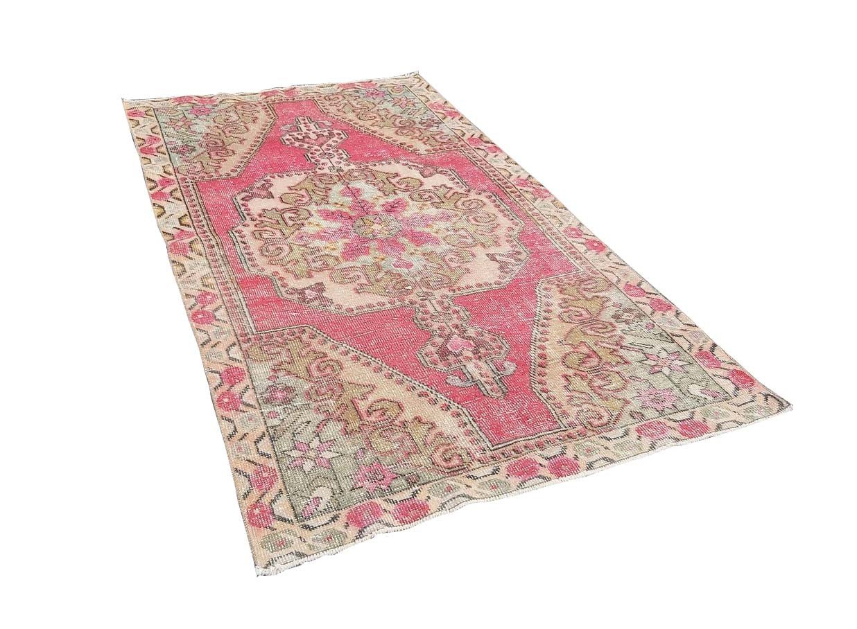 A vintage handmade Turkish wool rug featuring a central medallion pattern in pink and beige tones.