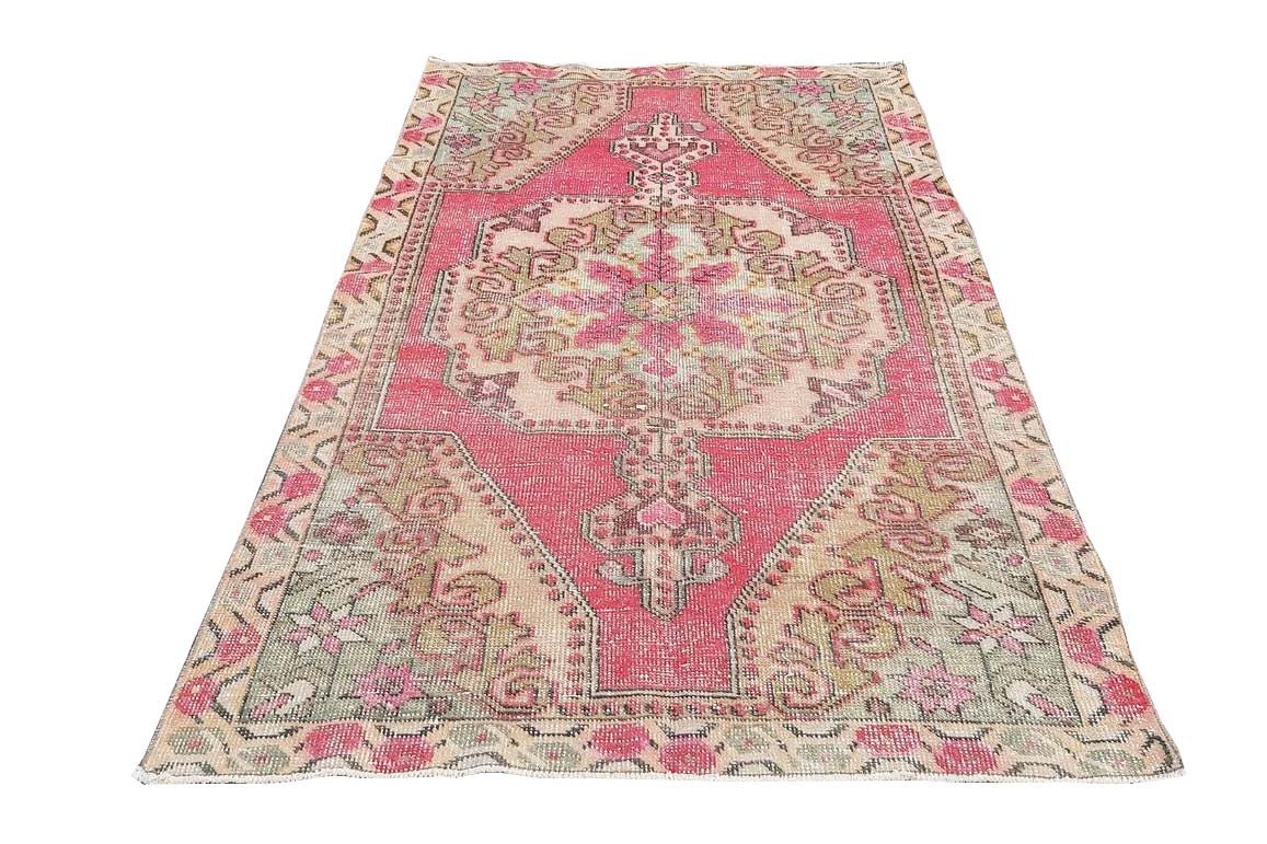 A vintage handmade Turkish wool rug featuring a central medallion in shades of pink and beige.