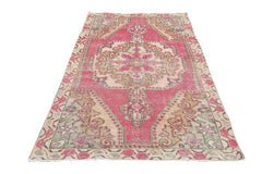 A vintage handmade Turkish wool rug featuring a central medallion in shades of pink and beige.