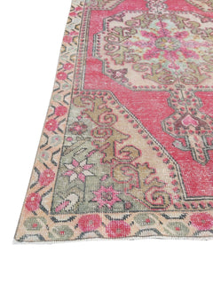 A vintage handmade Turkish wool rug featuring a pink field with intricate green and beige patterns.