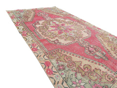 A vintage handmade Turkish wool rug featuring a central floral medallion in shades of pink and beige.