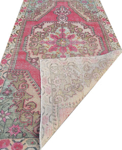 A vintage handmade Turkish wool rug featuring a pink and green geometric floral pattern.