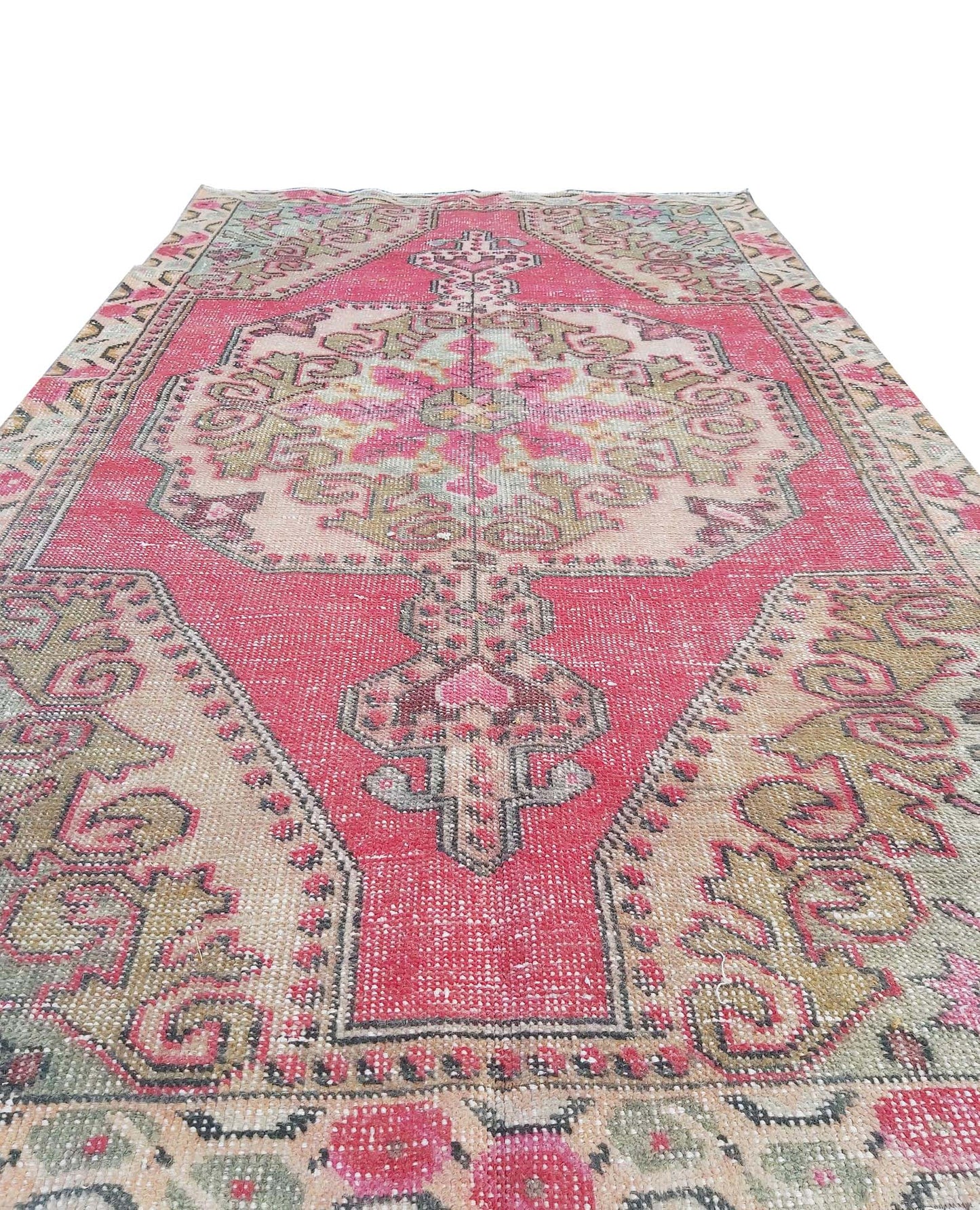 A vintage handmade Turkish wool rug featuring a central medallion in shades of pink and beige.