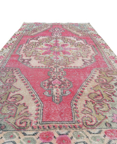 A vintage handmade Turkish wool rug featuring a central medallion in shades of pink and beige.