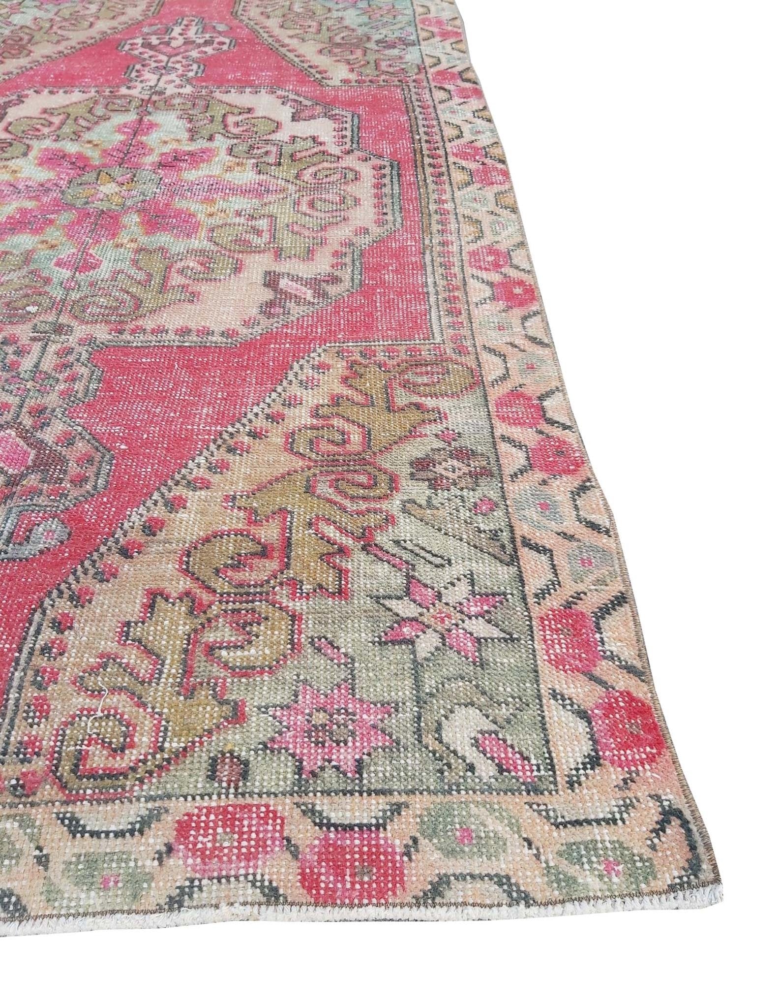 A vintage handmade Turkish rug featuring a geometric medallion pattern in shades of pink and green.