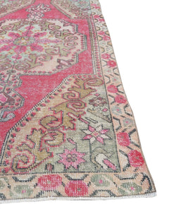 A vintage handmade Turkish rug featuring a geometric medallion pattern in shades of pink and green.