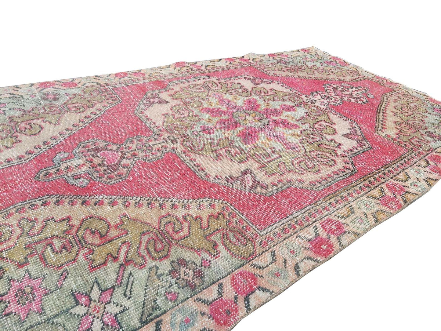 A vintage handmade Turkish wool rug featuring a central medallion in shades of pink and beige.