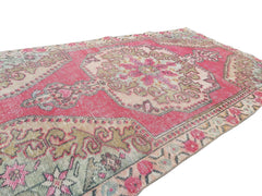A vintage handmade Turkish wool rug featuring a central medallion in shades of pink and beige.