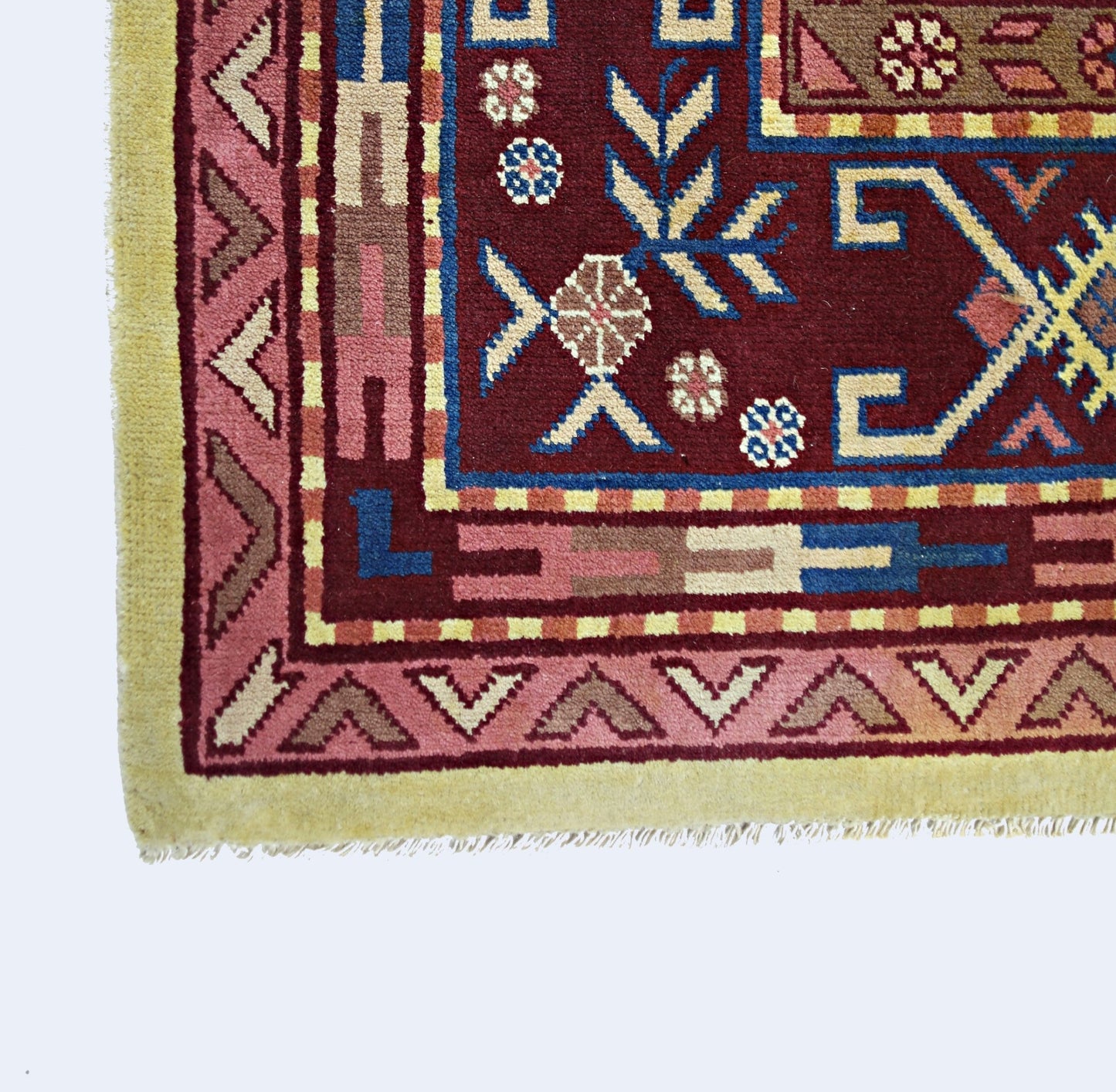A corner view of a vintage handmade Turkish rug featuring geometric patterns in red and blue.
