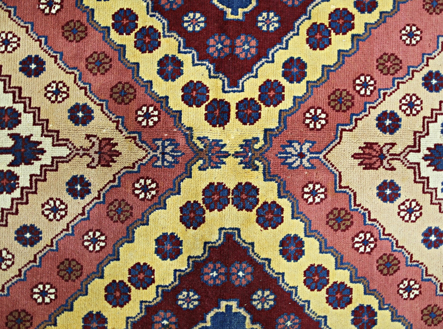 A vintage Turkish rug featuring a geometric pattern of floral motifs in red, yellow, and blue.