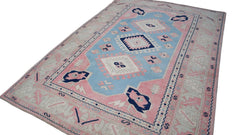 A vintage handmade Turkish Oushak rug featuring a blue central medallion on a pink field.