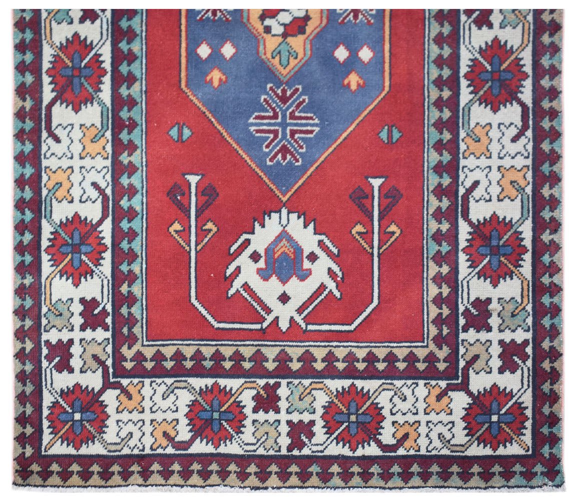 A vintage Turkish runner rug featuring a red field with a blue medallion and geometric patterns.