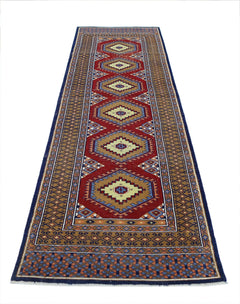 A vintage handmade wool runner featuring repeating geometric diamond motifs in red and tan.
