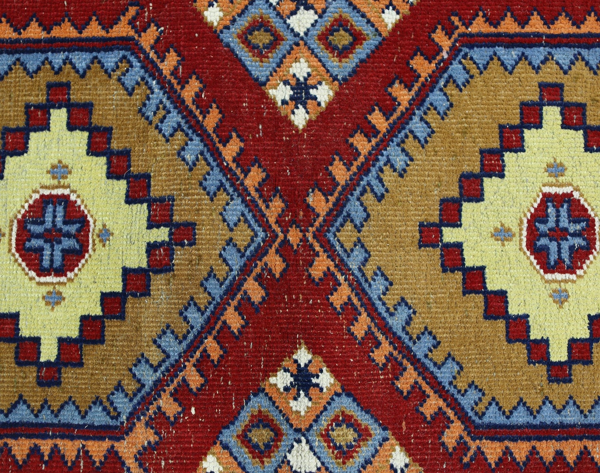 A vintage handmade wool runner featuring a geometric pattern of diamonds in red, gold, and blue.