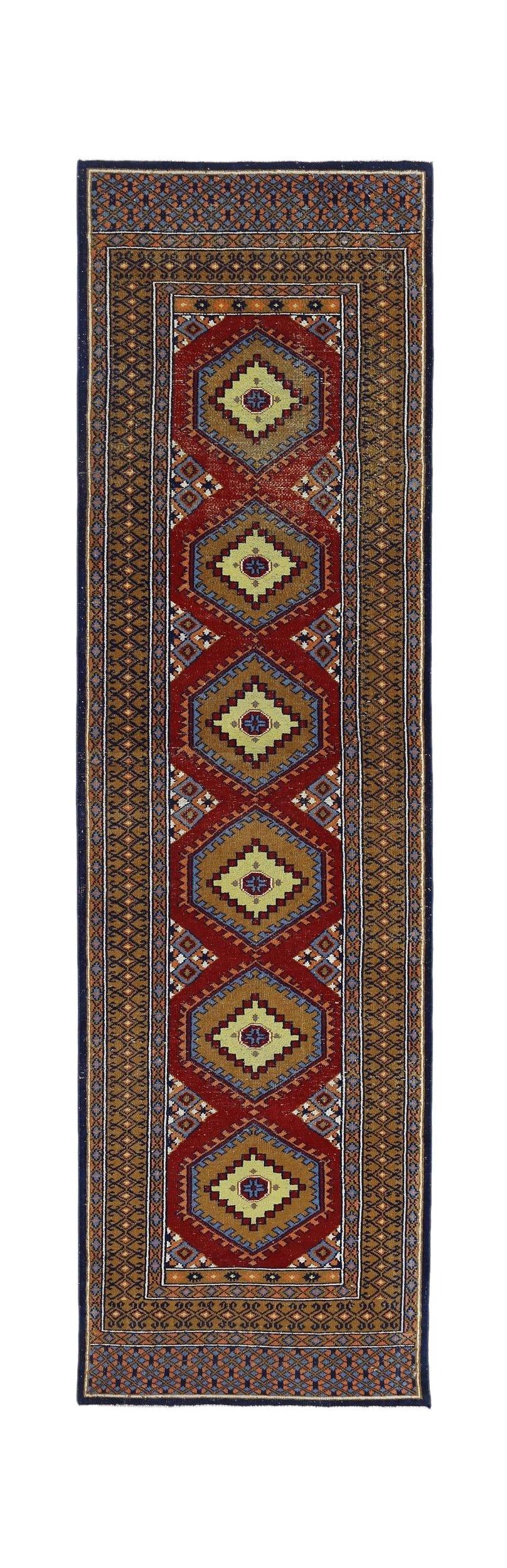 A vintage handmade wool runner featuring repeating geometric medallions on a deep red background.