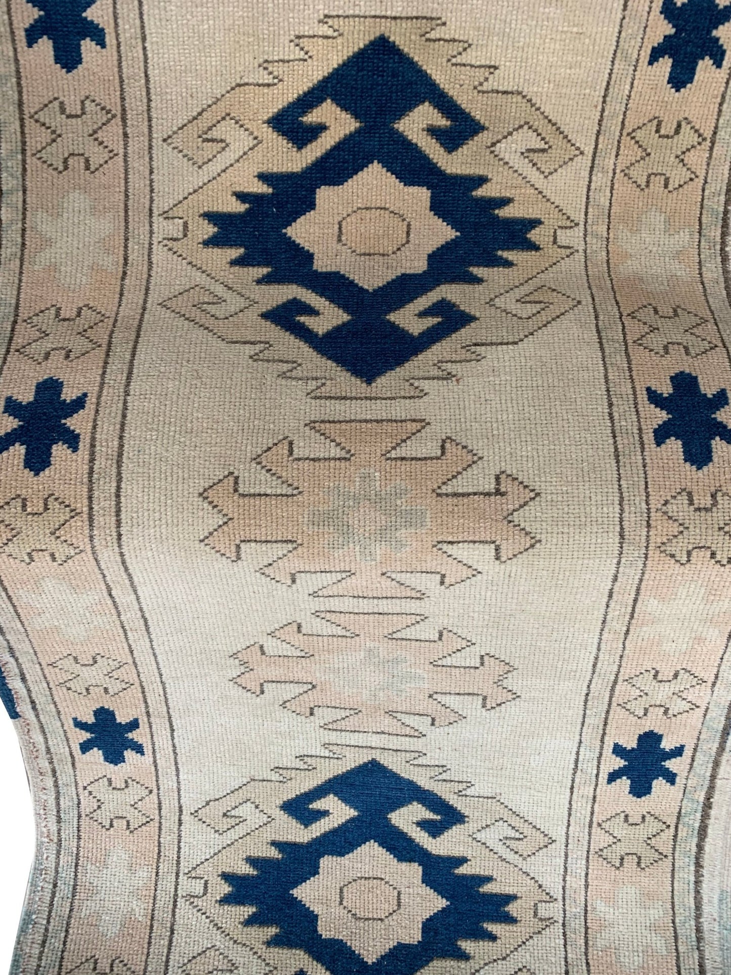 A vintage Turkish Oushak runner featuring blue geometric tribal motifs on a cream wool background.