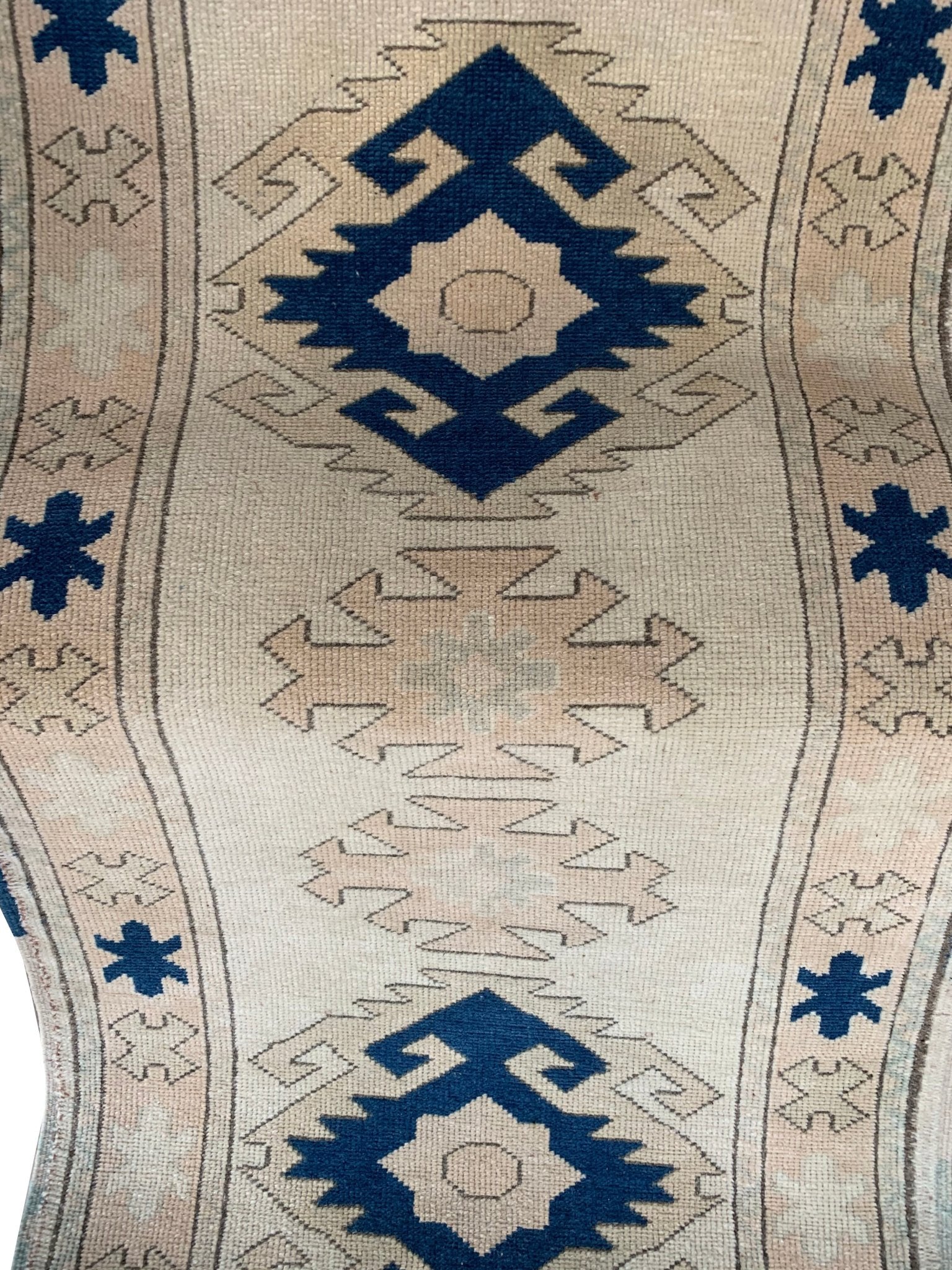 A vintage Turkish Oushak runner featuring blue geometric tribal motifs on a cream wool background.