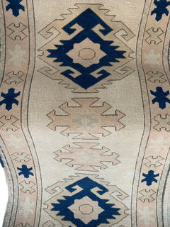 A vintage Turkish Oushak runner featuring blue geometric tribal motifs on a cream wool background.
