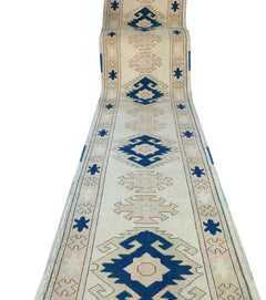 A vintage Turkish Oushak runner featuring blue geometric tribal motifs on a cream wool background.