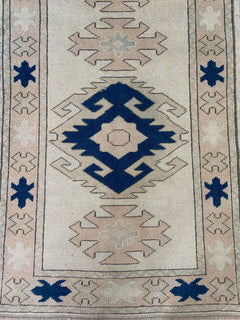 A vintage Turkish Oushak runner featuring a central blue geometric medallion on a cream field.