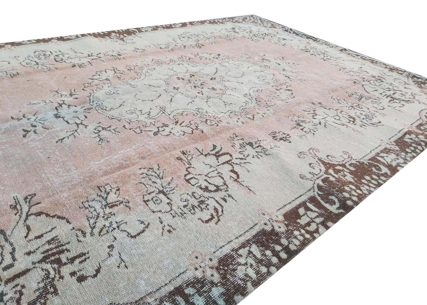 A vintage Turkish Isparta rug featuring a faded floral medallion in soft pink and brown tones.
