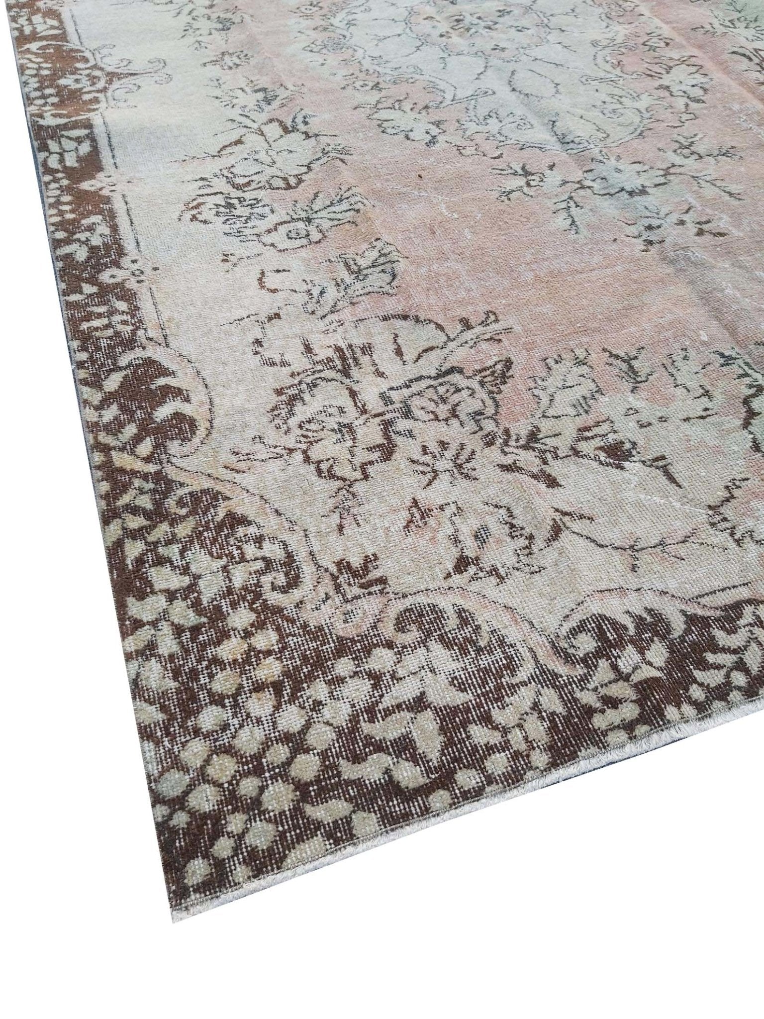 A vintage Turkish Isparta rug featuring a soft floral center and a dark brown patterned border.