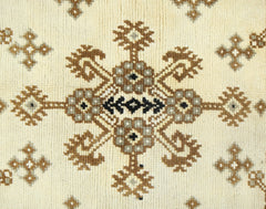 A vintage handwoven Afghan rug featuring a repeating geometric floral pattern in brown and cream.