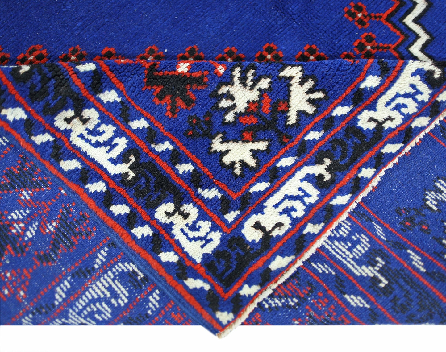 A folded corner of a vintage Turkish wool rug featuring a vibrant blue background with intricate red, black, and white geometric patterns.