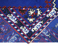 A folded corner of a vintage Turkish wool rug featuring a vibrant blue background with intricate red, black, and white geometric patterns.
