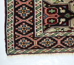 A corner view of a vintage Turkish prayer rug featuring geometric patterns in red, blue, and green.