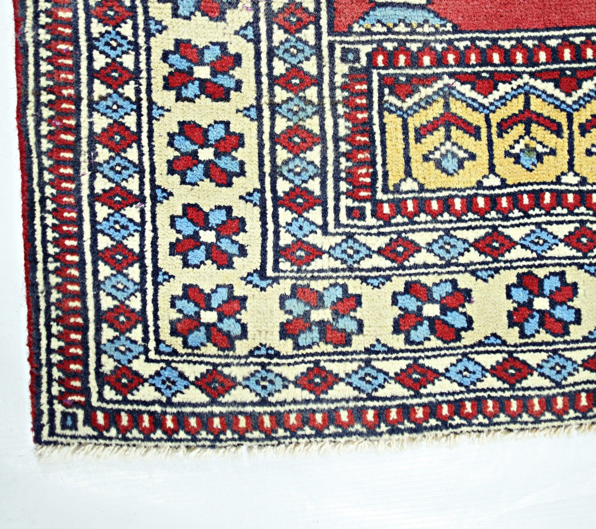 A corner view of a vintage Turkish Kayseri rug featuring geometric floral patterns in red and blue.