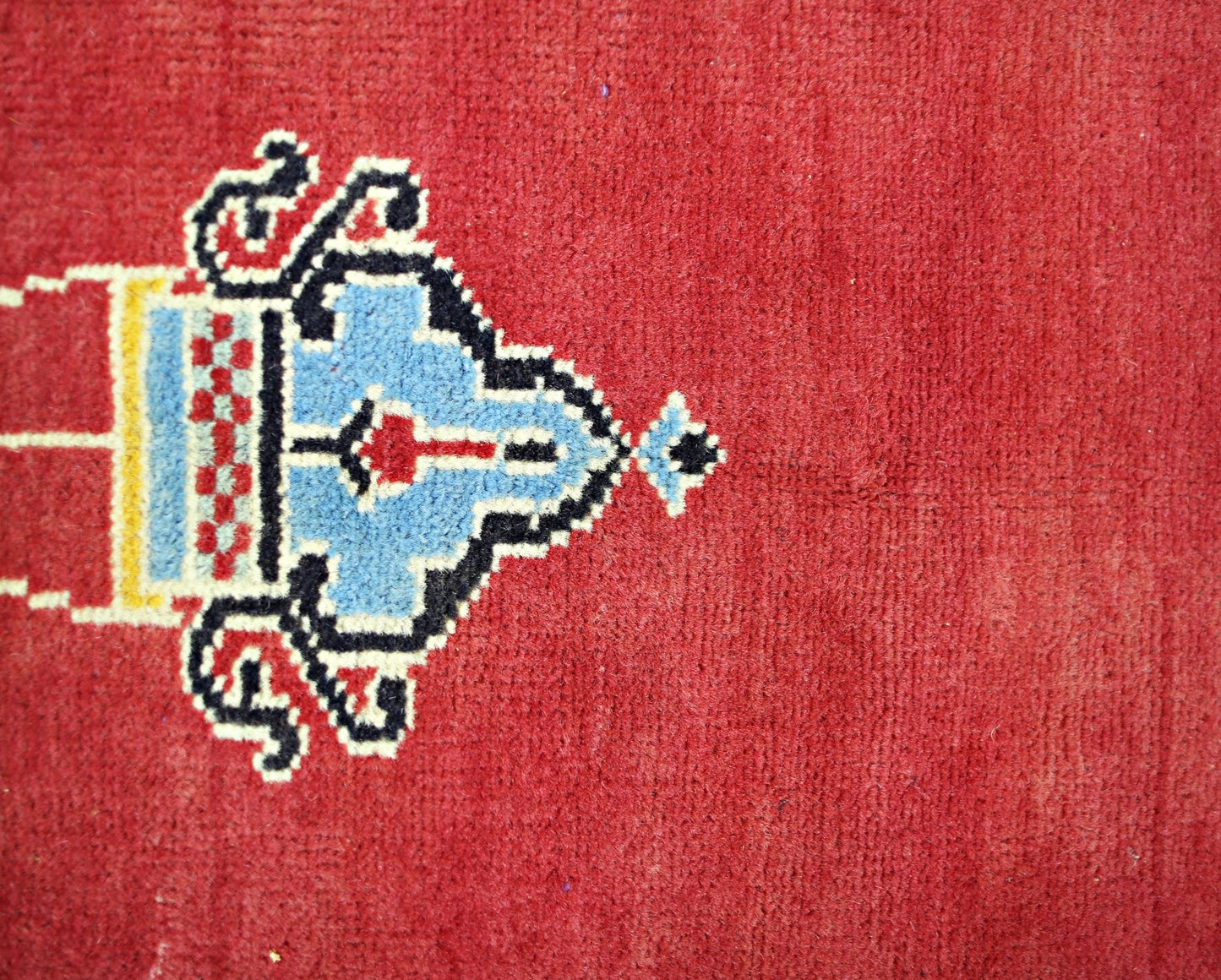 A close-up of a vintage Turkish Kayseri rug featuring a blue and red geometric motif on a red field.
