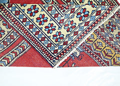 A folded vintage Turkish Kayseri rug featuring intricate geometric patterns in red, blue, and cream.