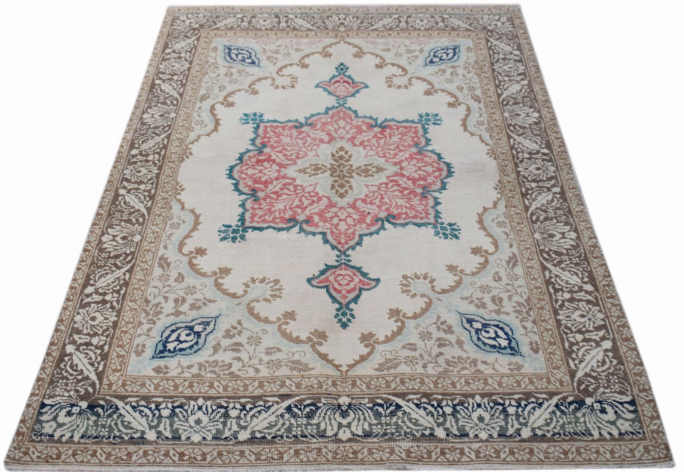 A vintage handwoven Turkish rug featuring a central pink floral medallion on a cream background.