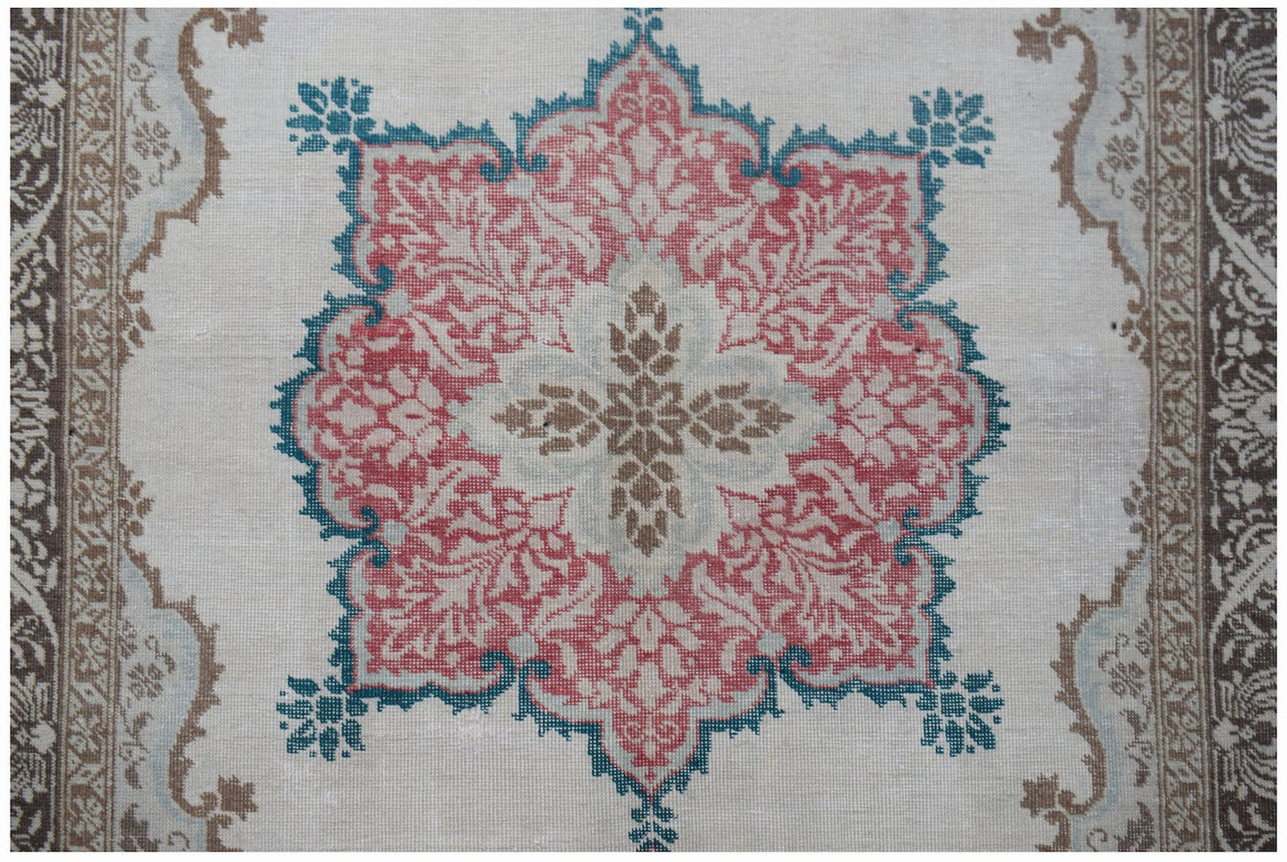 A vintage handwoven Turkish rug featuring a central floral medallion in red, teal, and brown.
