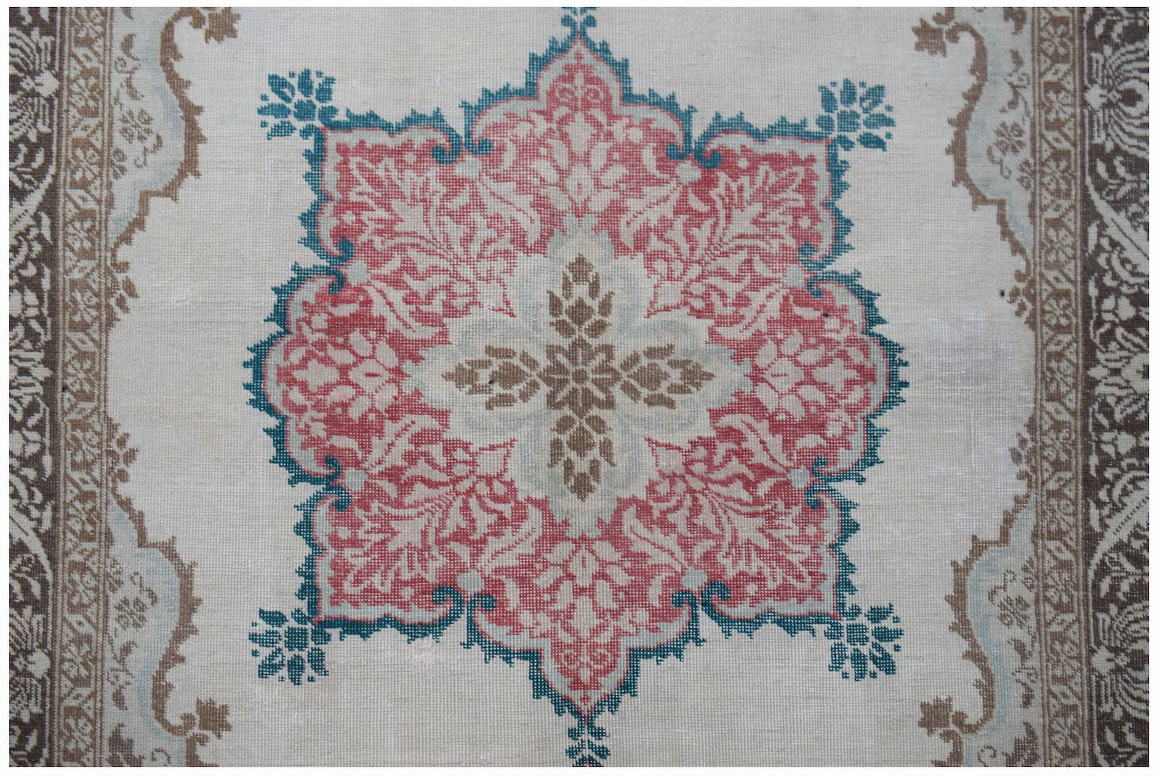 A vintage handwoven Turkish rug featuring a central floral medallion in red, teal, and brown.