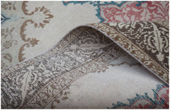 A vintage Turkish rug with a floral pattern in muted red, blue, and brown on a cream background.