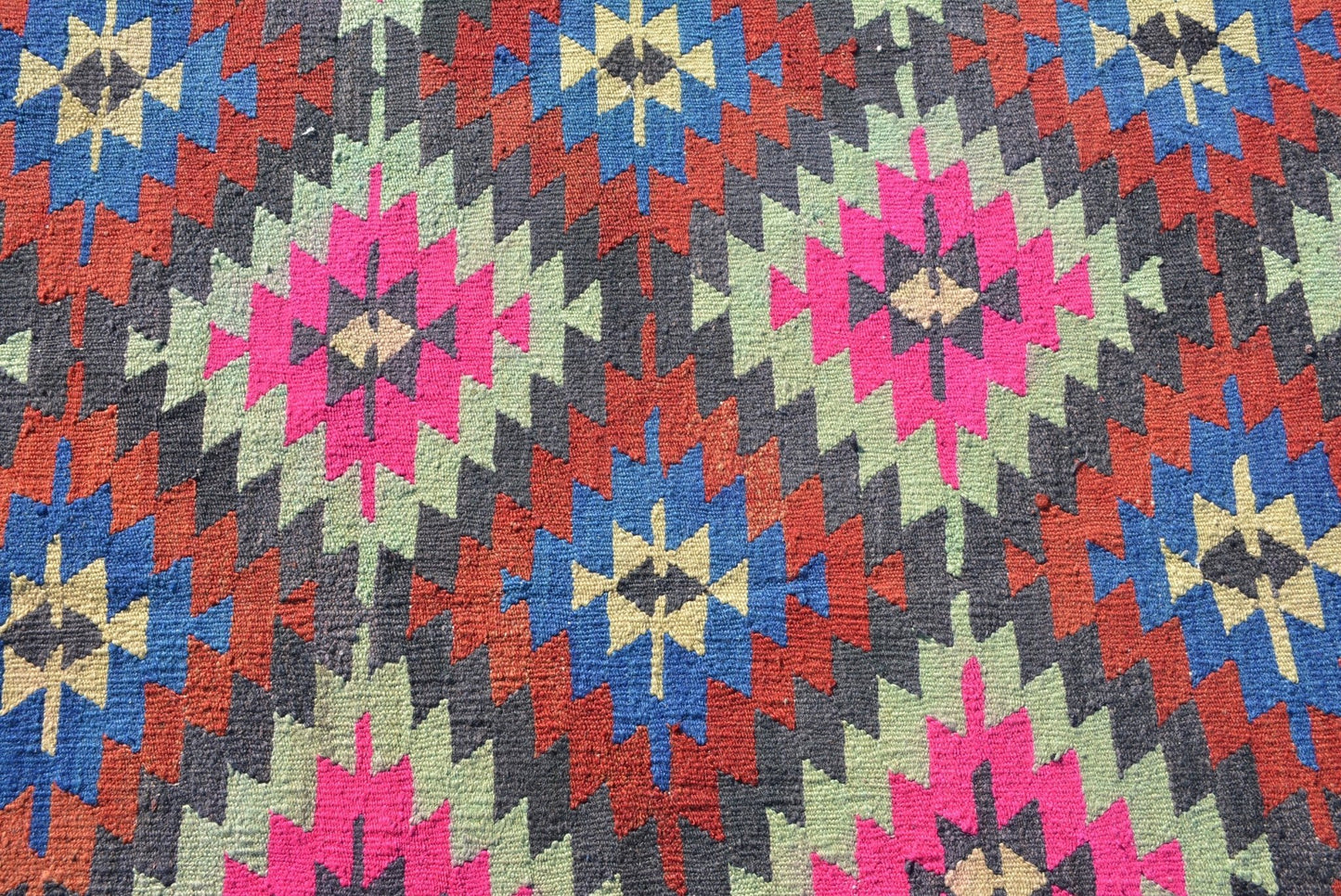 A vintage Turkish kilim rug featuring a geometric pattern in vibrant neon and earthy tones.