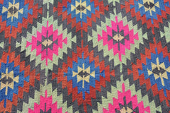 A vintage Turkish kilim rug featuring a geometric pattern in vibrant neon and earthy tones.