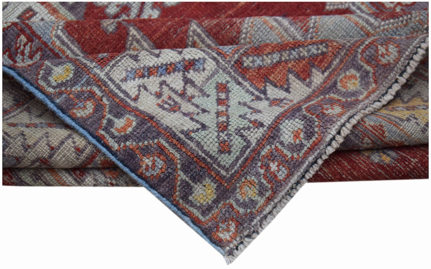A folded vintage Turkish Kula rug featuring geometric patterns in red, blue, and cream wool.
