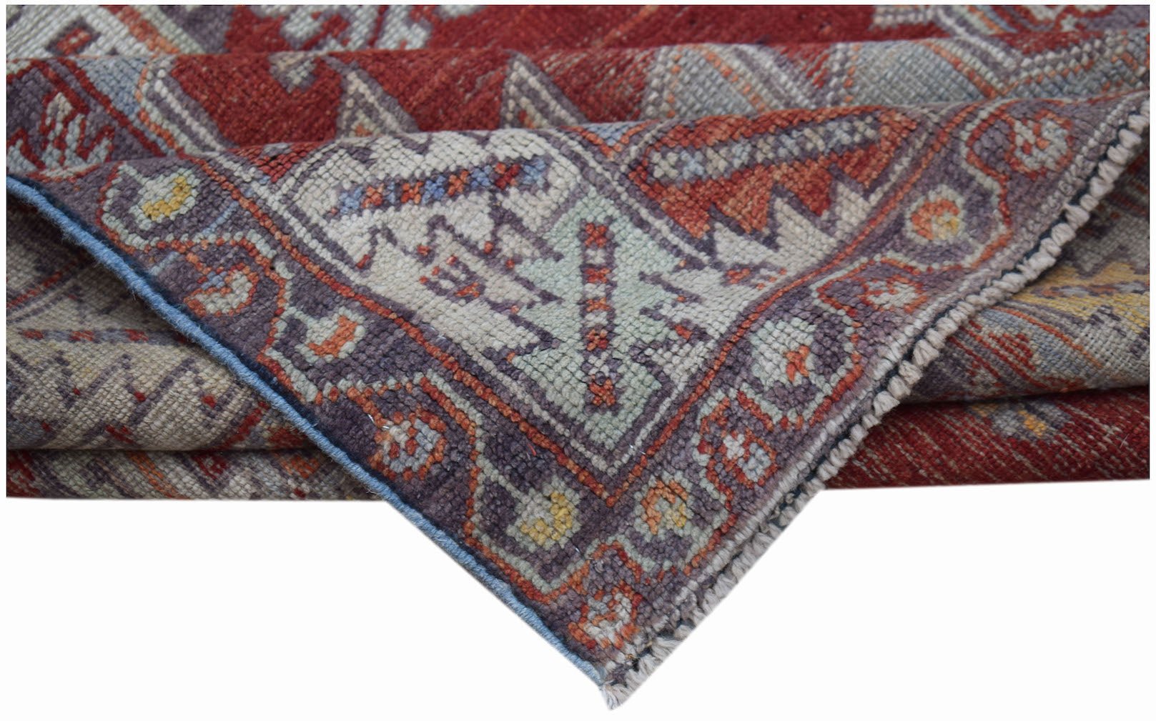 A folded vintage Turkish Kula rug featuring geometric patterns in red, blue, and cream wool.