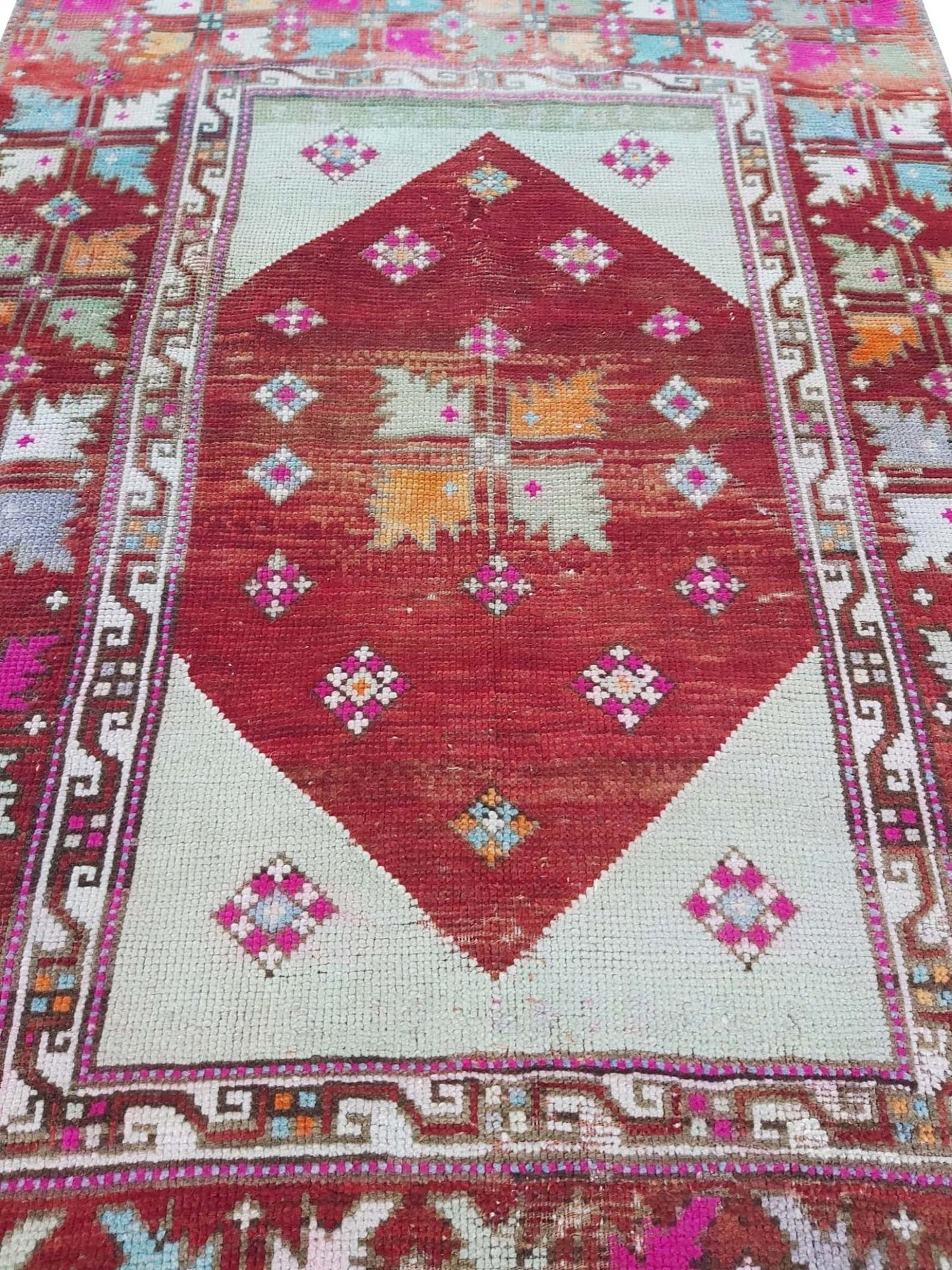 A vintage Turkish Kula rug featuring a red diamond medallion with geometric patterns on a light field.