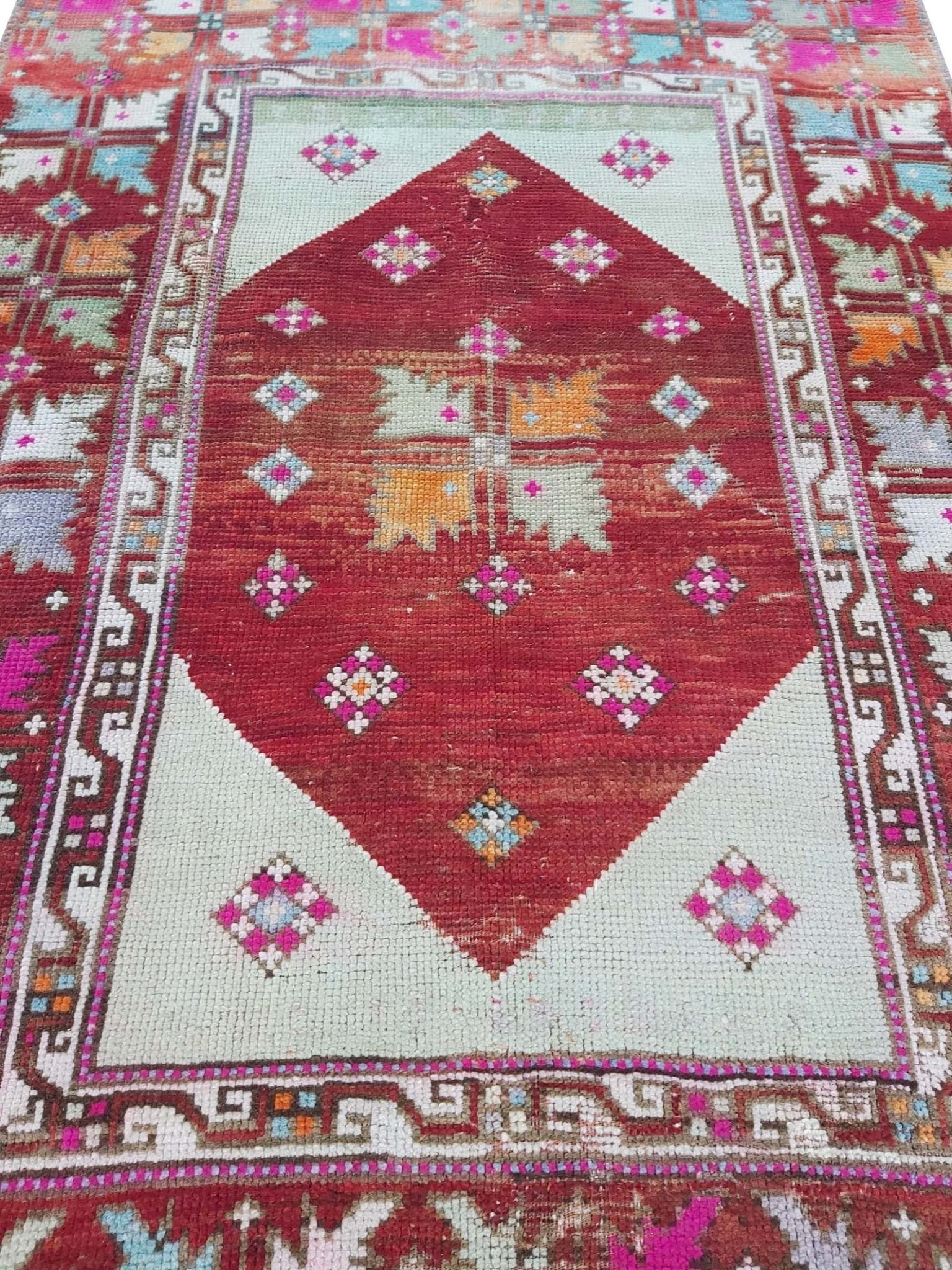 A vintage Turkish Kula rug featuring a red diamond medallion with geometric patterns on a light field.