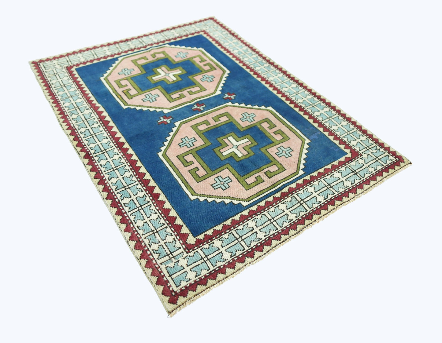 A vintage handmade Turkish rug featuring two geometric pink and green medallions on a blue field.